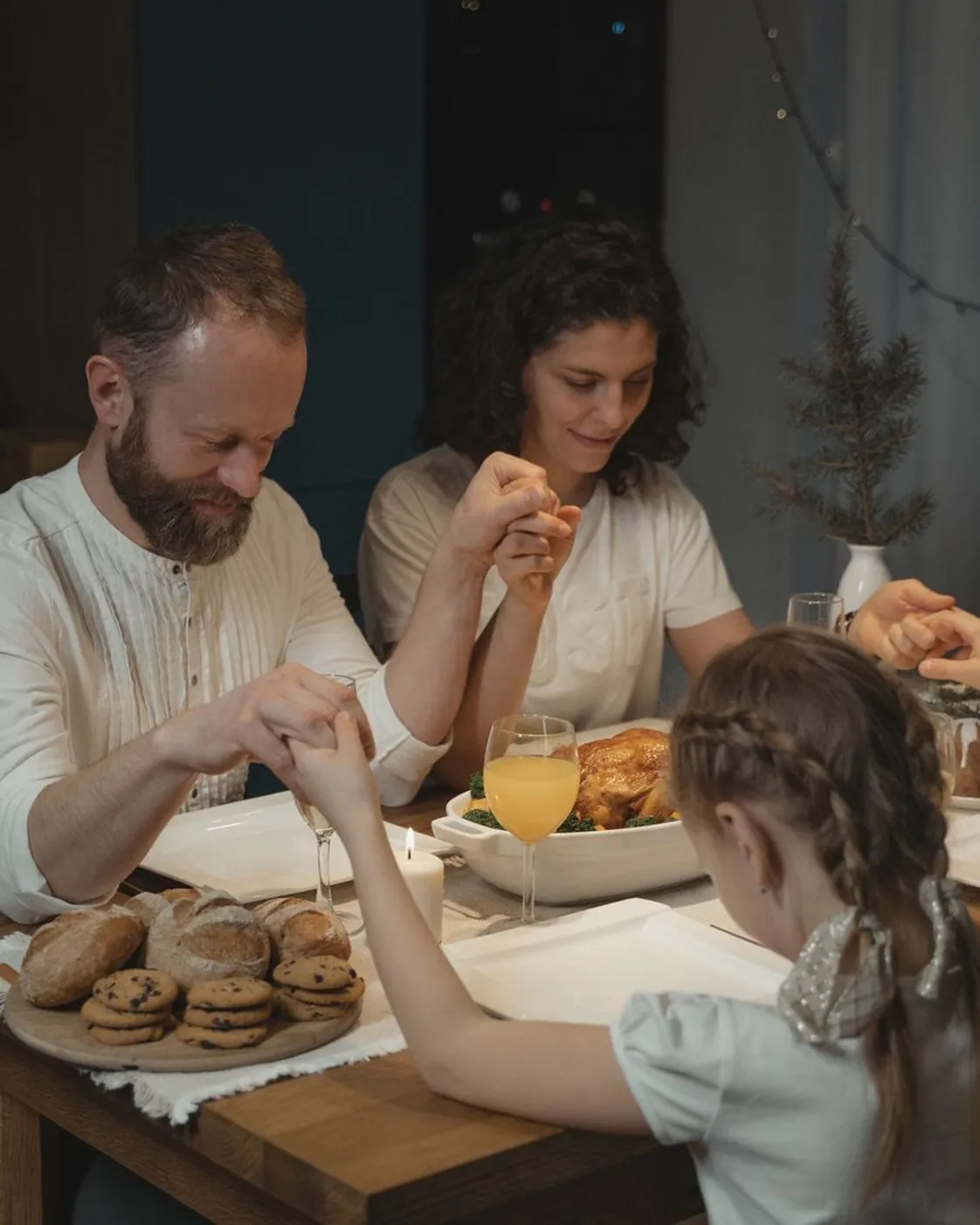 Family joins hands in prayer in a wooden home with warm light
